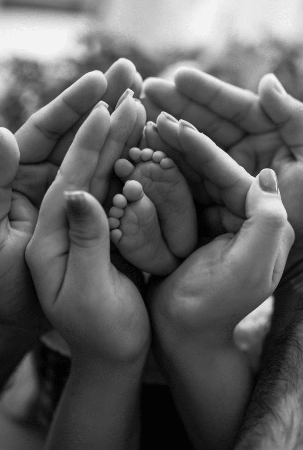 Black and white photo of two sets of hands holding small baby feet.