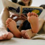 adult and children's feet shown while both people are reading a book
